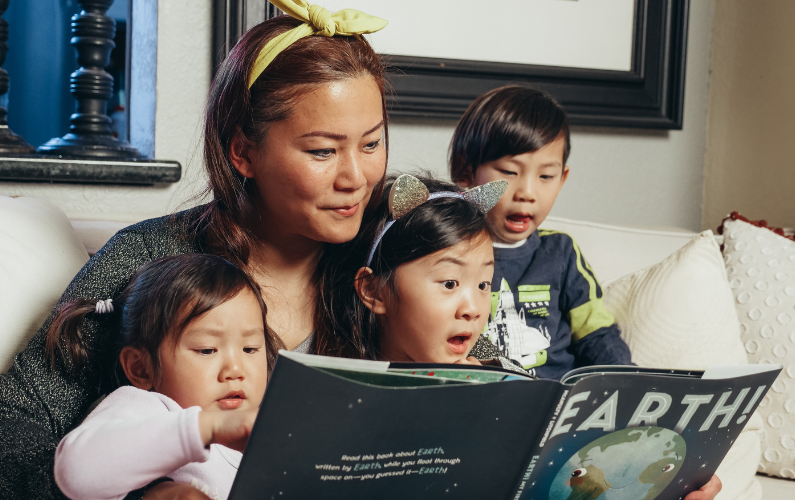 mother reading with 3 small children in her lap, looking in wonder at the book.